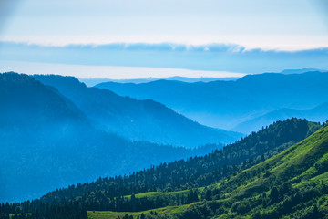 View over the Green Valley, surrounded by high mountains on a clear summer day. Layers of mountains in the haze during sunset.