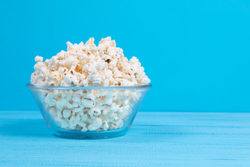 popcorn in a glass bowl on a blue table. popcorn with copy space