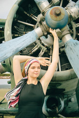 Attractive young stewardess (female flight attendant) posing hands up with aircraft screw of vintage airplane in airdrome
