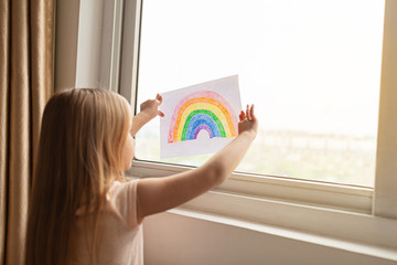 Kid painting rainbow during Covid-19 quarantine at home. Girl near window. Stay at home Social...