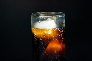 A glass of cola with ice cubes on black background