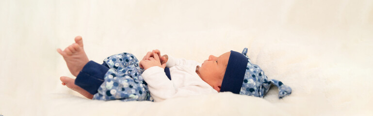 kleiner Junge liegt auf weißer Decke, blaue Hose und Haube, Baby