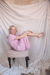Obraz premium Full length photo of gorgeous woman 20s in pink dress sitting in soft armchair with legs crossed and seductively holding finger at lips isolated over blue background