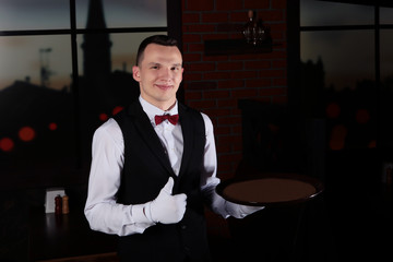 A white-gloved waiter holds a fist with his thumb up. Photo in the restaurant interior.