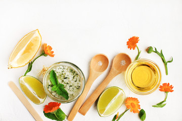Homemade skin care scrub with fresh herbs of mint, calendula, lime slices, olive oil, sea salt. Natural ingredients top view lay out over white table. Making organic cosmetics.