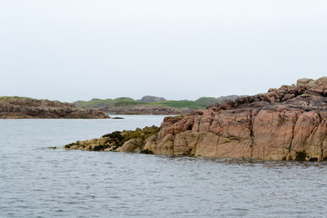 Textured volcanic rocks emerging from the water surface in the northern sea of Scotland. Shot taken from the ferry boat from Mull island and The little and wild Staffa island