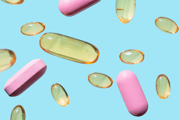 .Transparent yellow medical capsules and pink pills on light blue background.