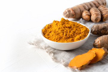 Curcuma powder in bowl and fresh turmeric root on white . Healthy spice immunity. Close up. Natural antiseptic.