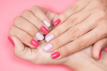 Obraz na płótnie Canvas Closeup photo of two female hands and fingers manicured. Fingernails with fresh professional spring or summer naildesign isolated on pastel pink background. Painted nails with modern gel-polish.