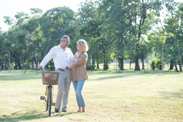 Cheerful active senior caucasian couple with bicycle walking through public park together. Perfect activities for elderly people in retirement leisure lifestyle