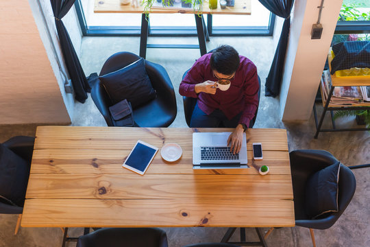 Top View Of Young Asian Freelancer Working From Home And Using Tablet While Sitting The Wooden Table.