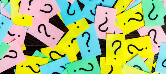 Too Many Questions on wooden background. Pile of colorful paper notes with question marks. top view