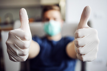 Young man with mask and gloves showing hands, thumbs up. Coronavirus, world pandemic. Stay at home.