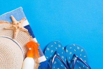 Summer beach flat lay accessories. Sunscreen bottle cream, straw hat, flip flops, towel and seashells on colored Background. Travel holiday concept with copy space