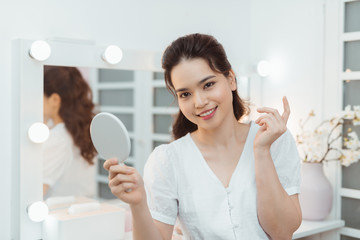 Smiling attractive brunette holding mirror in bright bedroom
