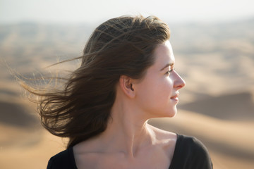 Caucasian young woman with long hair in a black dress at sunrise in the desert.