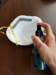 Closeup of lady spraying ethyl alcohol to mask.  Prevention of Coronavirus Covid-19 concept.