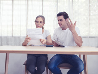 Fototapeta premium Young caucasian couple hand holding credit card and debt bill on table in home,men and women have overdue financial foreclosure problem sit in room with serious and unhappy payment.