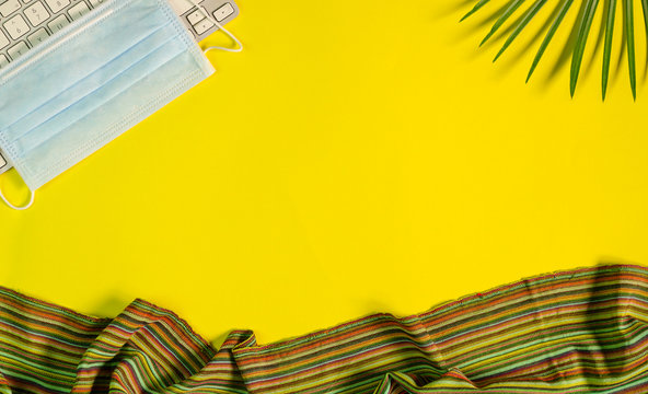 Top view of yellow color office table with keyboard, surgical face mask, palm leaves and fabric. - Powered by Adobe