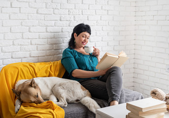 Charming middle aged woman enjoying being at home and reading sitting on the sofe