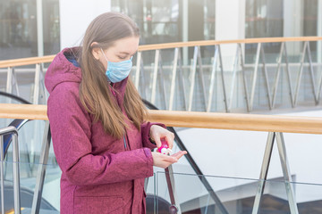 Viral disease prevention concept. Young woman in a medical protective mask using wash hand sanitizer gel as protection against virus and bacteria in shopping center.  Coronavirus prevention.