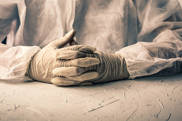 Doctor's hands in bio suit and gloves, folded on the table. Dramatic view