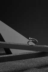 Subject shot of an unlocked silver ring made as a bent nail. The unusual ring is fixed on the gray grained surface surrounded with geometric-shaped objects in semi-darkness. 