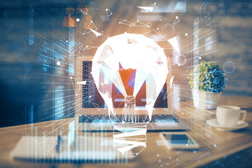 Computer on desktop in office with bulb icon hologram. Multi exposure. Concept of idea.