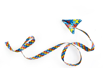 Autism awareness day or month. Paper plane in origami style with autism awareness puzzle ribbon on white background.