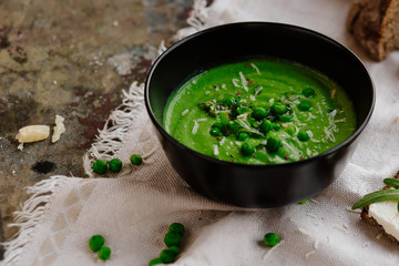 Green peas and spinach puree soup in a black bowl. Vegetarian cream soup on gray background. Healthy eating during quarantine