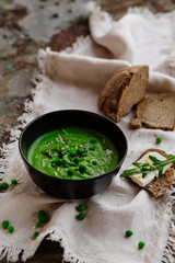 Green peas and spinach puree soup in a black bowl. Vegetarian cream soup on gray background. Healthy eating during quarantine