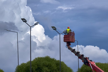 workers in lift bucket repair street light pole with double head and change the lighting to diode