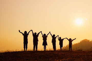 Silhouette of happy children standing with raised hands on the mountain at the sunset time.