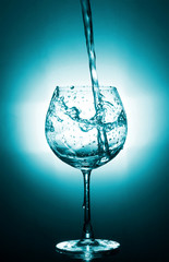 Motion of pouring splash water in transparent wine glass with reflect of blue light backdrop.