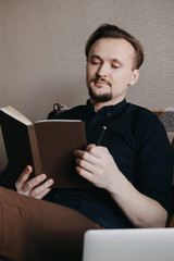 A young European guy in a dark blue shirt with a dark beard looks at a brown notebook that looks like a book. Home insulation. Home Office.