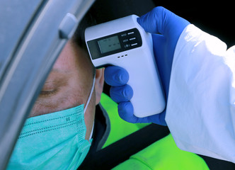 The doctor checks the body temperature for the presence of coronavirus at a checkpoint at the driver of the vehicle. Hand with a thermometerd with a thermometer