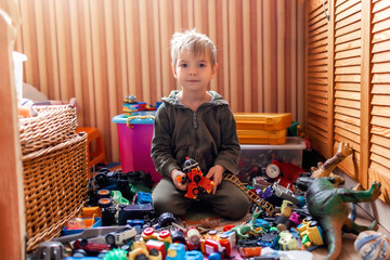 Cute preschooler boy sitting on the floor among plenty of toys, home activity during lockdown