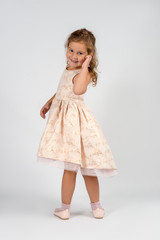 A little smiling girl wearing  beautiful beige  elegant dress stands on a white background in the studio