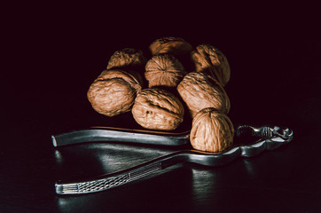 Walnuts with nutcracker over black background.