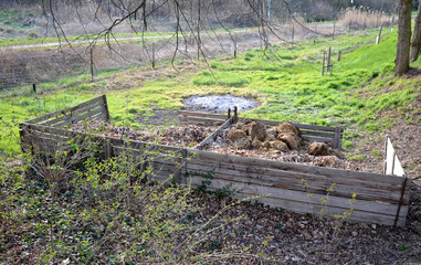 Two large wooden composting boxes of corral in a meadow under trees to store manure leaves and...