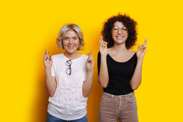 Fototapeta na wymiar Caucasian curly haired women are dreaming about something crossing fingers on a yellow wall with free space