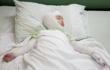 Obraz na płótnie Canvas Asian baby girl lying sick with bandaged head and arm on bed at hospital. Baby girl with head and arm injuries. Real life.