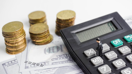 Selective focus on figurine of businessman on calculator with money and coins in background.  Tax savings concept. 