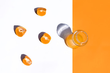 top view crystal glass with orange juice on white and orange background, four orange segments on the white, horizontal