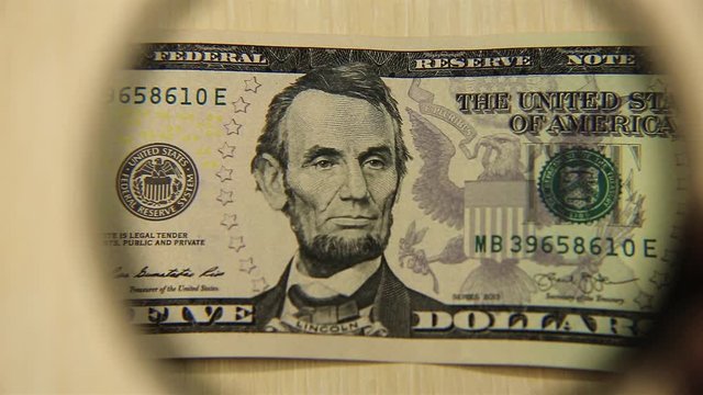 View a five American dollar bill lying on a table with a magnifying glass. concept of business and finance