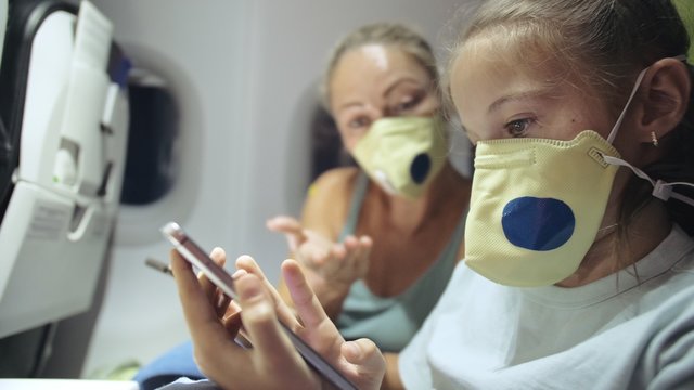 Family Woman And Child Baby Travel Tourist Caucasian At Plane Aircraft With Wearing Protective Medical Mask. Use Smartphone Mobile. Health Virus Protect Coronavirus Epidemic Sars-cov-2 Covid-19.