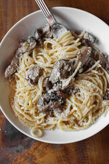 Mushroom white pasta topped with parmesan on a white plate and on top of a wooden table. 