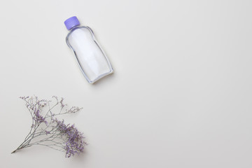 purple cosmetic bottle and flower on light yellow background with copy space