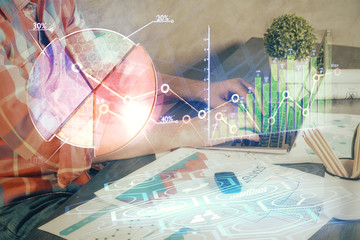 Double exposure of stock graph with businessman typing on computer in office on background. Concept of hard work.