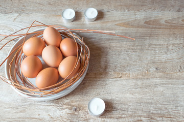 Raw brown eggs on a plate with candles on wooden rustic background. Easter concept, mockup, top view. 